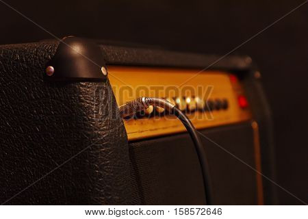 Combo amplifier for electric guitar with inserted input jack on the black background. Shallow depth of field low key close up.