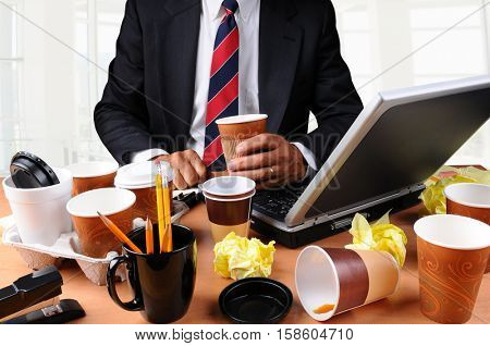 Closeup view of a very cluttered businessmans desk. Man is holding a coffee cup and crumpled papers litter his workspace. HIgh Key Office Background.