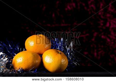 Christmas Tangerine Or Mandarin With New Year Tinsel On A Dark Red Background