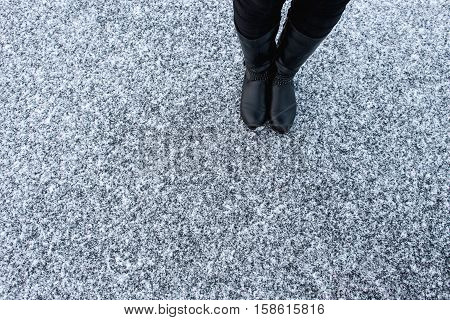 Women black leather boots standing on rough snow background. Gritty snow covered asphalt surface. Textplace. Top view