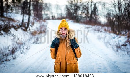 girl in a yellow jacket outside the city in the winter woods on a snowy road