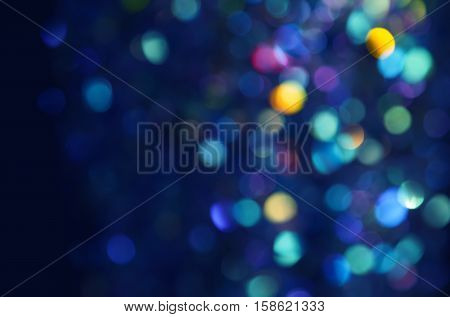 Colorful beautiful blurred bokeh background with copy space. Holiday texture. Glitter multicolored light spots on navy blue backdrop defocused