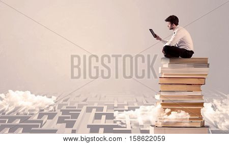 A businessman with laptop tablet in elegant suit sitting on a stack of books on top of sandy labirynth background concept