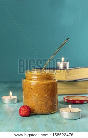 A photo of a jar of madrono, wild strawberry, fruit butter, with a spoon, madrone berries, candles and old books. Selective focus