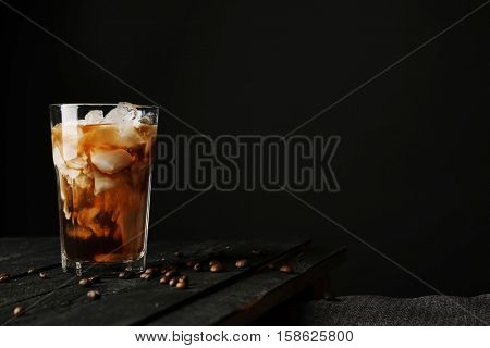 Pouring cream into a glass with iced coffee on table and black background