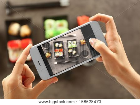 Woman taking photo of tasty sushi set