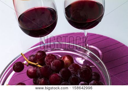 red wine in the wine glass grape in the vase on the glass table