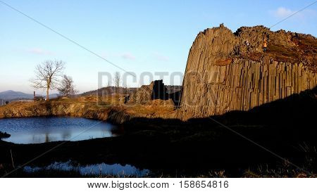 A small lake next to the rock with nice clear blue sky and some trees around.