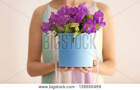 Woman holding box with purple bellflowers on light background