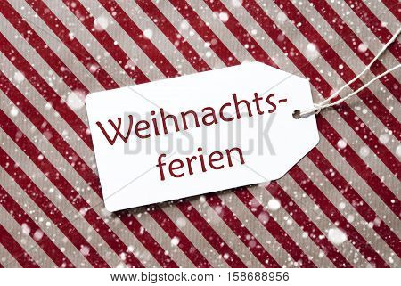 One Label On A Red And Brown Striped Wrapping Paper. Textured Background With Snowflakes. Tag With Ribbon. German Text Weihnachtsferien Means Christmas Break