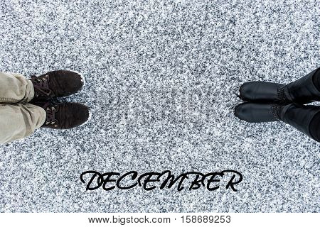 Male and Female boots standing at heart symbol with text december on asphalt covered gritty snow surface. Rough snowy. Winter love. Top view. Relations concept