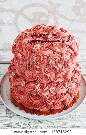Gorgeous two-tier cake covered in roses made of butter cream icing sitting on a cake pedestal with background