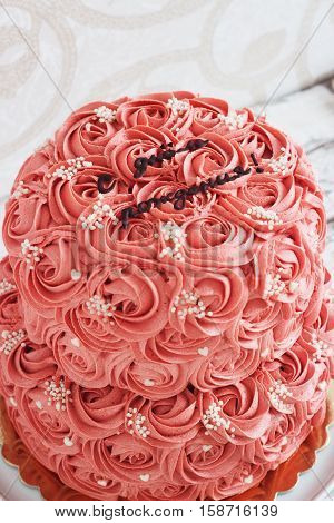 Gorgeous two-tier cake covered in roses made of butter cream icing sitting on a cake pedestal with background