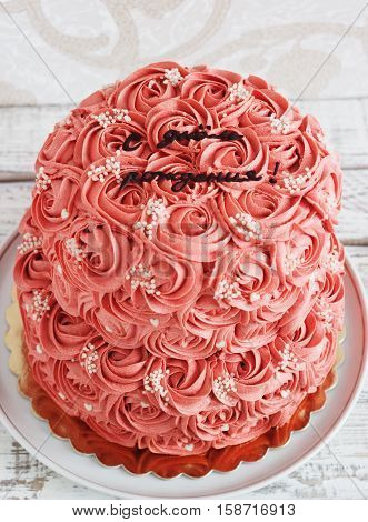 Gorgeous two-tier cake covered in roses made of butter cream icing sitting on a cake pedestal with background