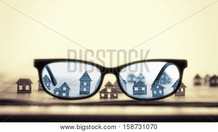 Eyeglasses lie on the open newspaper with paper houses. That could mean rent search purchase real estate.