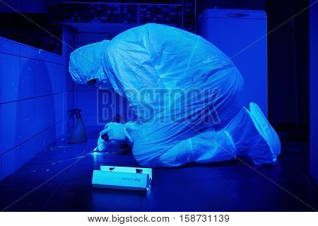 Criminologist collecting DNA on place of bloody crime under UV light