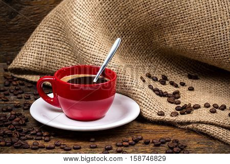 Coffee cup with metallic spoon and surrounding coffeebeans and gunny textile