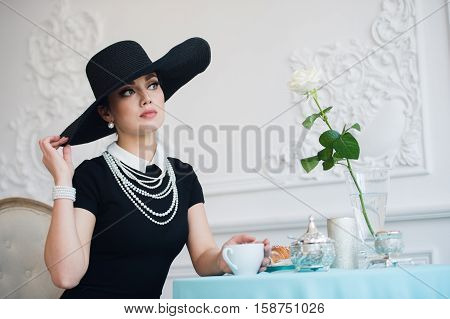 Woman in hat, much like the famous actress, croissant eating and drinking tea
