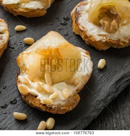Canape or crostini with toasted baguette ricotta cheese pears walnuts nuts Siberian pine and honey on a slate board. Ideal as an aperitif. Square image. Selective focus