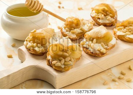 Canape or crostini with toasted baguette ricotta cheese pears nuts Siberian pine and honey on a wooden board. Ideal as an aperitif. Selective focus