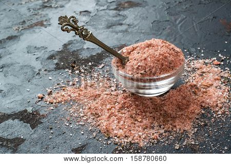 Special pink Adygei salt with spices (Russia) in a glass salt shaker and spoon on a dark textured background. Prepared according to the old recipe with garlic and spices. Useful economically spent