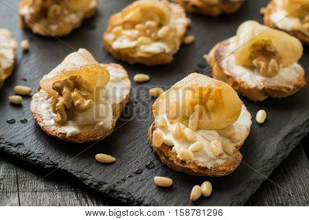 Canape or crostini with toasted baguette ricotta cheese pears walnuts nuts Siberian pine and honey on a slate board. Ideal as an aperitif. Selective focus shallow DOF