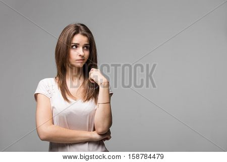 Portrait of contused thinking brunette woman. Studio shot on gray background.