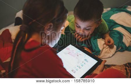 Little brother and sister sitting in pajamas using a digital tablet on Christmas Eve