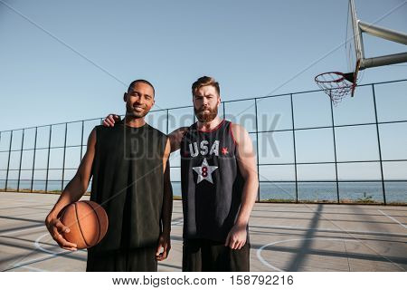 Two young basketball players standing together at the playground and looking at camera
