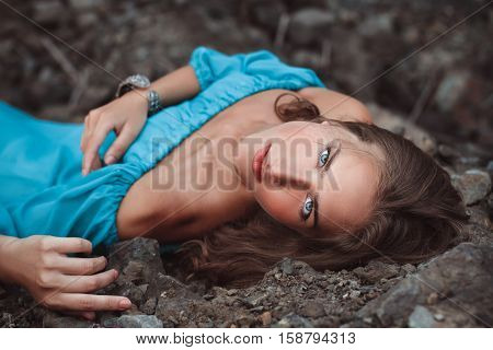 beautiful dreamy blonde girl with blue eyes in a light turquoise dress lying on the stones
