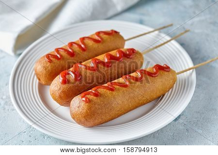 Corn dog traditional American corndog street junk food deep fried hotdog meat sausage with ketchup snack treat coated in a thick layer of cornmeal batter on stick unhealthy eating on rustic table.