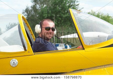 Smiling pilot sitting in the cockpit of a light aerobatic plane with the canopy open