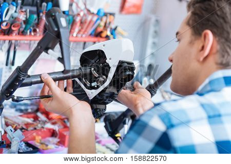 Nice job. Young handsome ambitious man holding drone details and discovering them while sitting in a workroom.