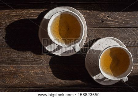 two cups of tea tea in a ceramic bowl white pottery in brown speckled cups from clay cups and saucers on a dark background