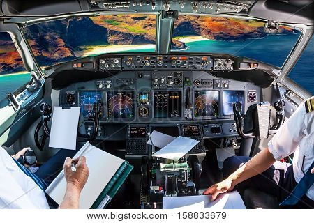 Airplane cockpit flying on Na Pali coast, Kauai, Hawaii, United States, with pilots arms and blank white papers for copy space.