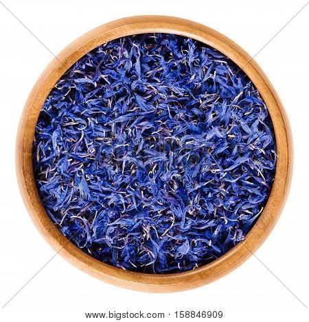 Dried cornflowers in wooden bowl. Edible flowers of Centaurea cyanus with intense blue pigment, used for tea and salad decorations. Isolated macro food photo close up from above on white background.