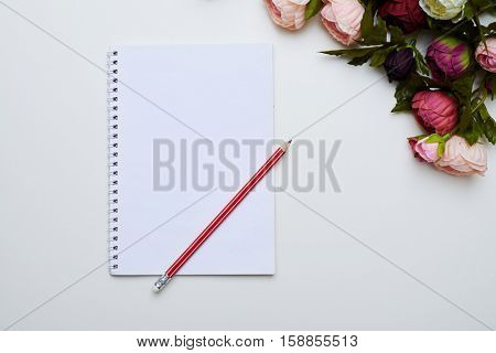 A mid shot of ring-bound notebook and red long pencil on it. Splendid peonies placing on right side above