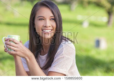 Beautiful happy Asian Eurasian young woman or girl outside drinking mug of tea or coffee