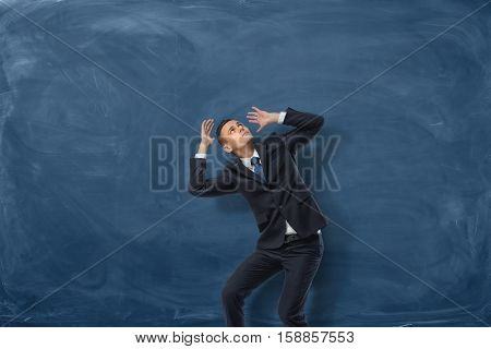 Businessman standing in desparate pose on blue chalkboard background. Problems and issues. Protection and defense. Psychological burden and stress.