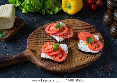 Healthy sandwhiches with fresh ricotta cheese, tomatoes and parsley on whole grain rye bread. Side view, front focus