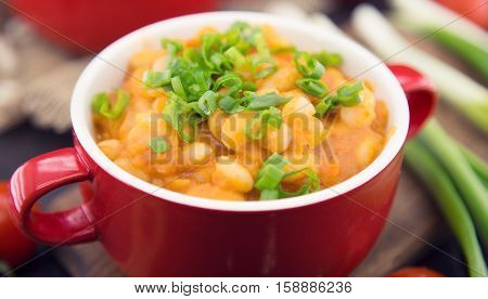 White beans in tomato sauce in a red ceramic bowl on rustic wooden table. Organic food.