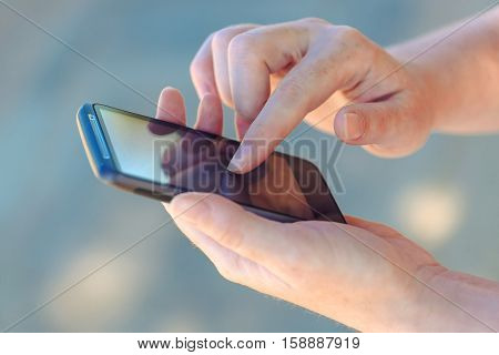 Close up of female hands using smartphone device with touchscreen outdoors to access open wireless internet network from hotspot