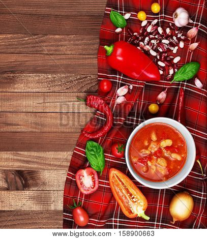 Soup Chili con carne on wooden background surrounded by vegetables.