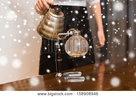 equipment, coffee shop, people and technology concept - close up of woman with pot pouring hot water to coffeemaker filter at cafe bar or restaurant kitchen over snow