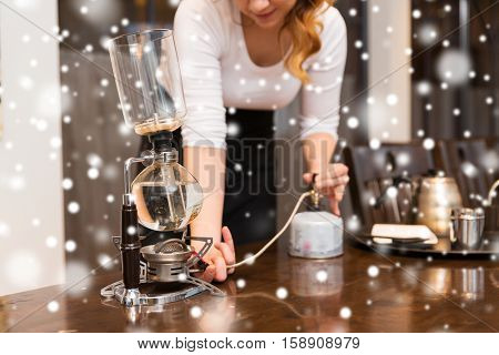 equipment, coffee shop, people and technology concept - close up of woman with butane gas burner heating water in siphon coffeemaker at cafe bar or restaurant kitchen over snow