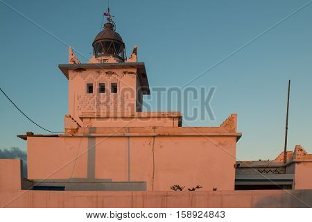 Walls of the lighthouse colored into an orange color by the sunset light. Blue early evening sky. Tower with a light still off. Sidi Ifni Morocco.