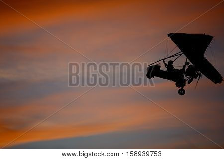 Hang glider flying in sky opposite sun at sunset