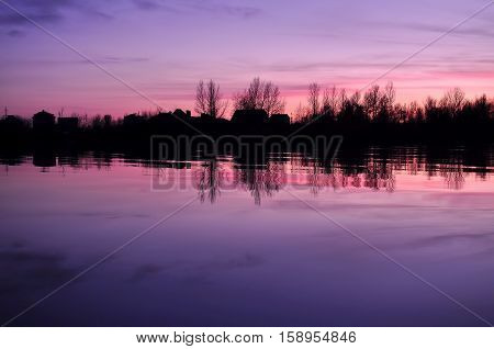 Beautiful Colorful Dusk On A River With Silhouettes Of Houses And Trees