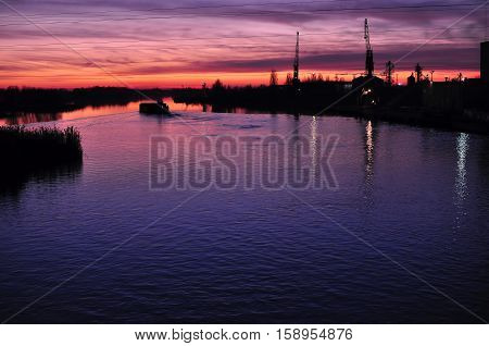 Beautiful Colorful Dusk On A River With Silhouettes Of Barge And Cranes.