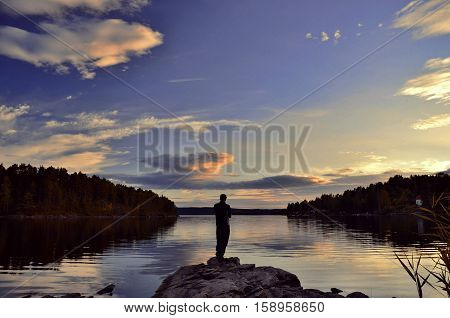 One man standing ashore lake during sunset